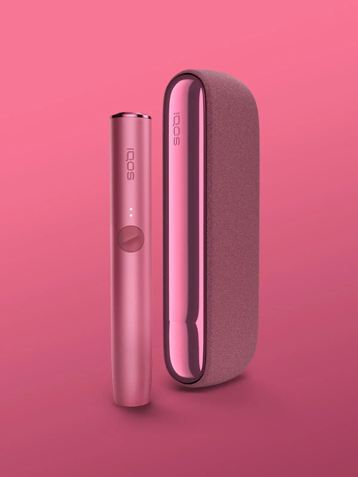 An IQOS ILUMA in Sunset Red colour, standing in front of a pink/sunset red background with its TEREA stick holder standing next to the charging case.